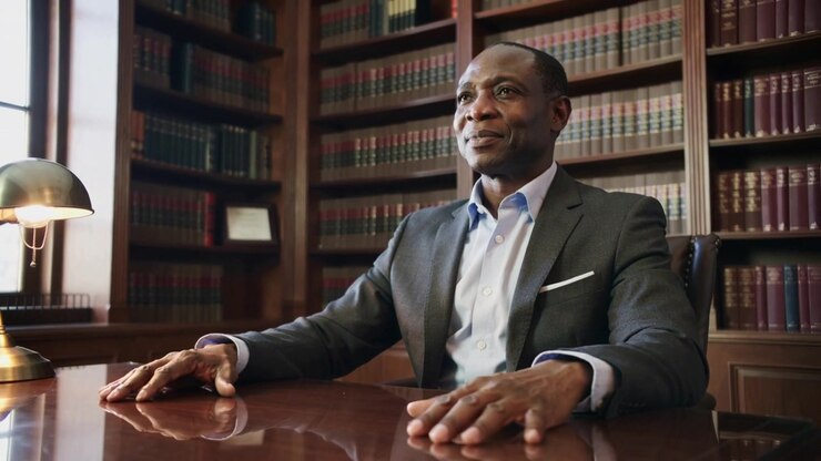 After off-camera question, man in dark suit placing palms on polished desk in office, brass lamp