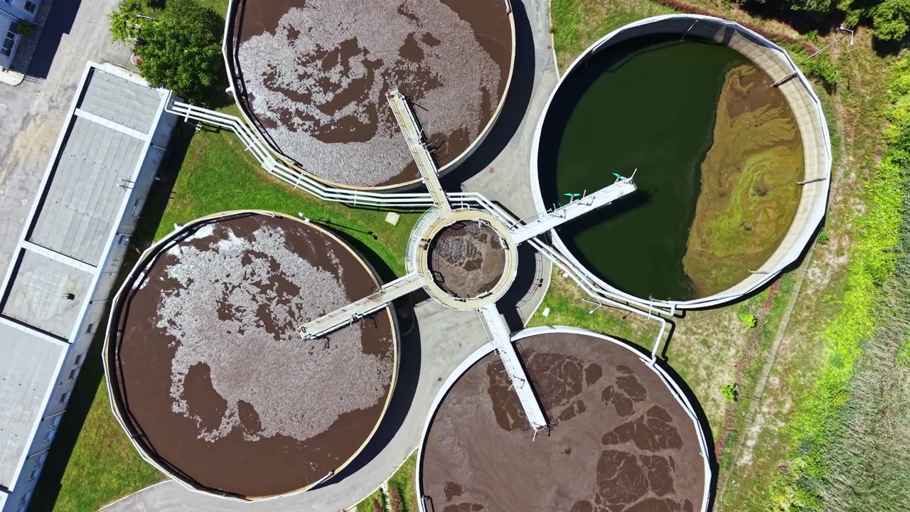 Gran planta de tratamiento de aguas residuales que muestra varios tanques de tratamiento en funcionamiento durante un día soleado con cielos despejados.