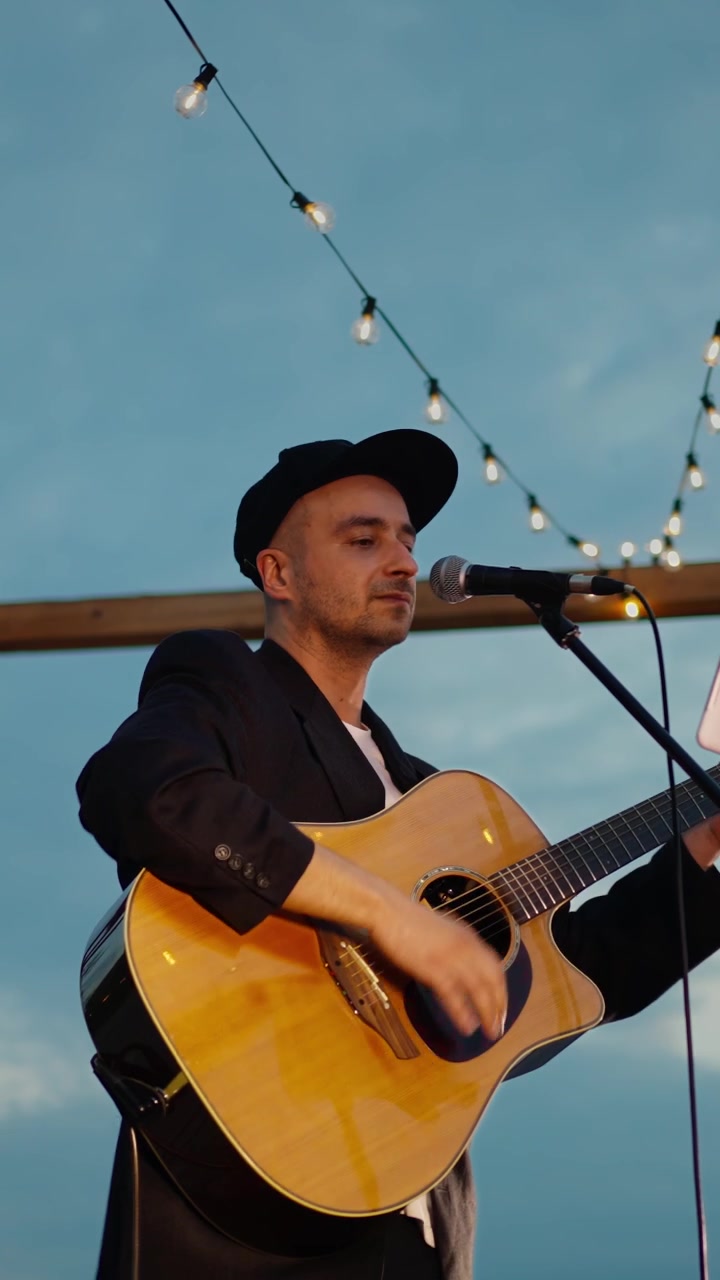 Mandlig singer-songwriter spiller akustisk guitar og synger udendørs