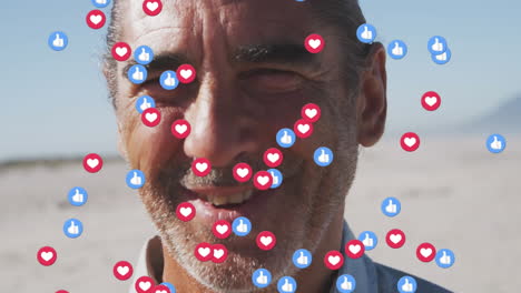 animation of thumbs up and heart icons over portrait of smiling senior man on beach