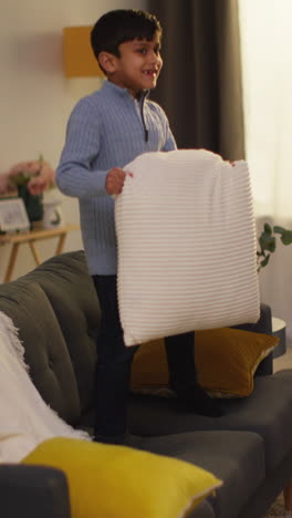 Vertical-Video-Of-Disruptive-Young-Boy-Behaving-Badly-At-Home-Jumping-On-Sofa-And-Throwing-Cushions-Around-Lounge