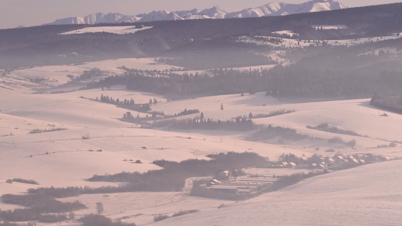 Slow tilt up over beautiful snow covered landscape with small villages, forests and mountains