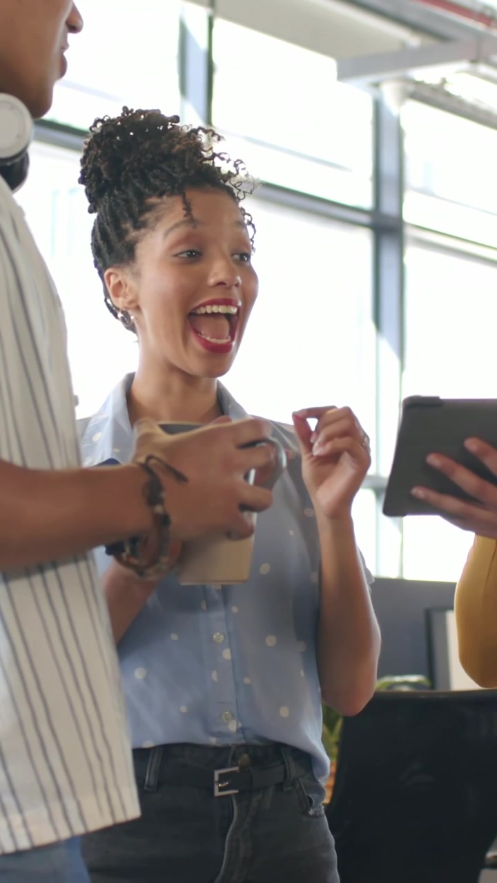 Vertical video: Reacting to tablet woman in blue blouse gesturing to screen at window, holding mug