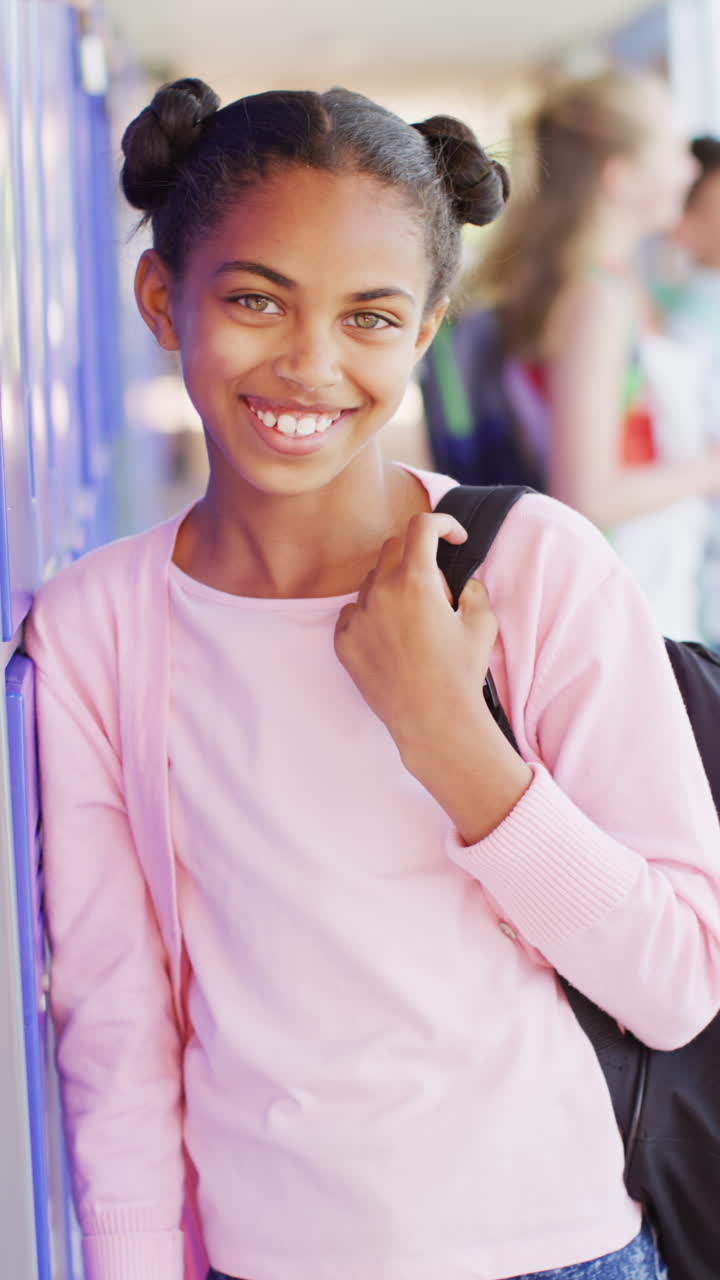 Vertical video of portrait of happy biracial schoolgirl in school