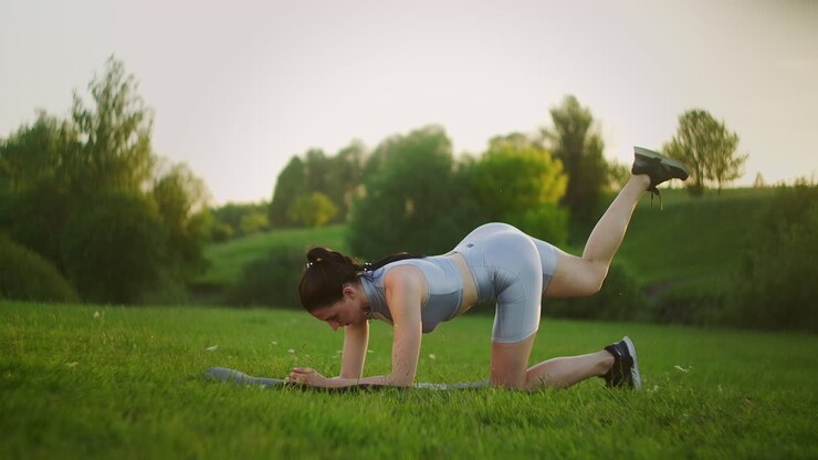 Woman athlete involved in fitness in park doing leg lifts on mat. Workout. Work on a beautiful body in the morning or at sunset. Exercises for leg and hip muscles