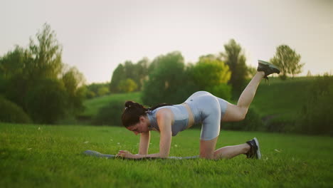 woman athlete involved in fitness in park doing leg lifts on mat. workout. work on a beautiful body in the morning or at sunset. exercises for leg and hip muscles