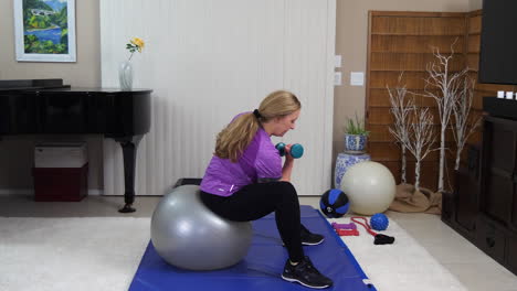 mature woman performing arm curls while sitting on exercise ball, side view, static