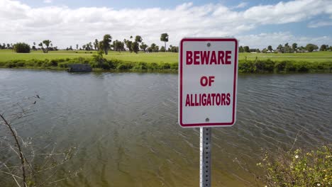 Cuidado-Con-El-Cartel-De-Los-Caimanes-Por-El-Estanque-Ondulante-Y-El-Paisaje-Verde,-La-Sartén-Circular