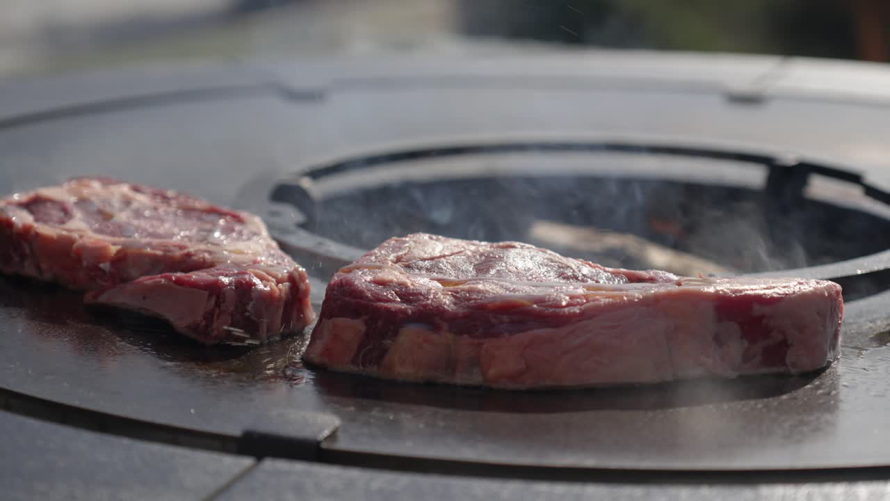 oil being poured ontop of raw steaks cooking on a BBQ to help them cook