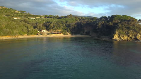 Aerial-Drone-Shot-Flying-Away-from-Spiaggia-Zuccale-Beach,-Elba,-Italy-on-a-Calm-Sunset-Evening