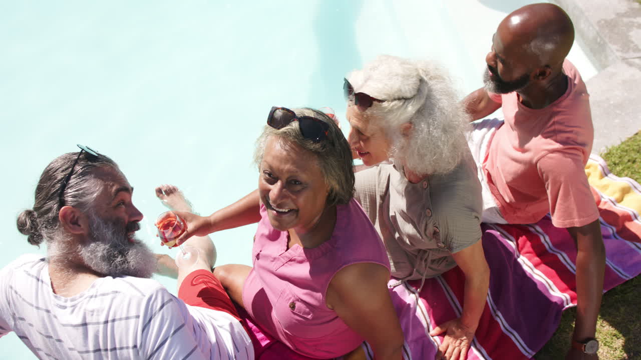 Enjoying poolside, senior friends laughing and toasting with drinks, having fun together