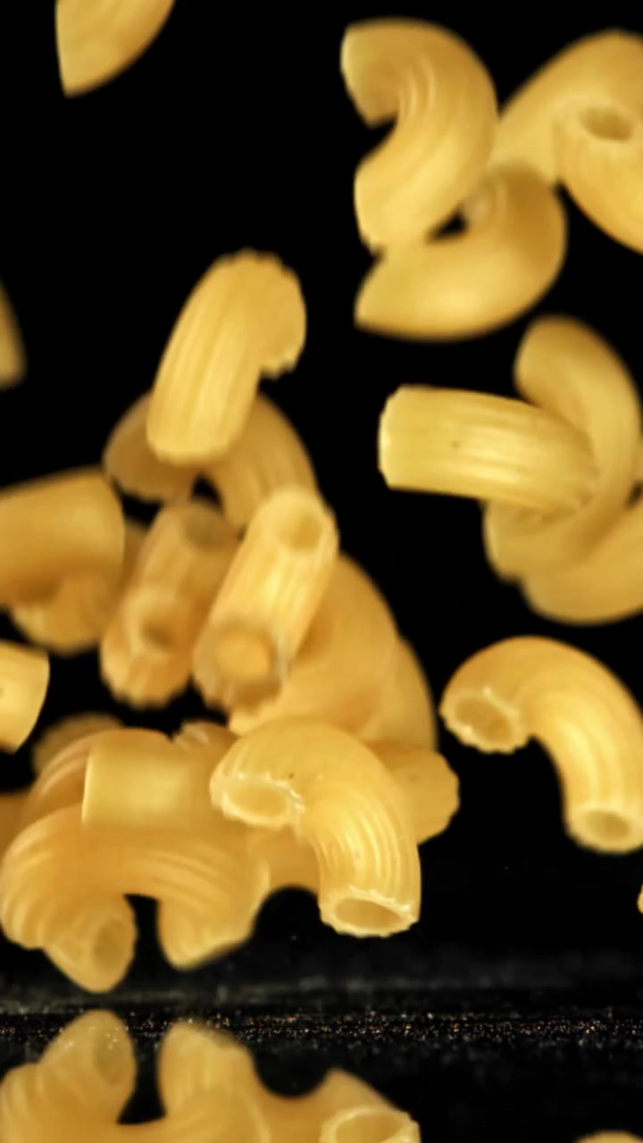 Pasta maccheroni secca che cade al rallentatore su sfondo nero.