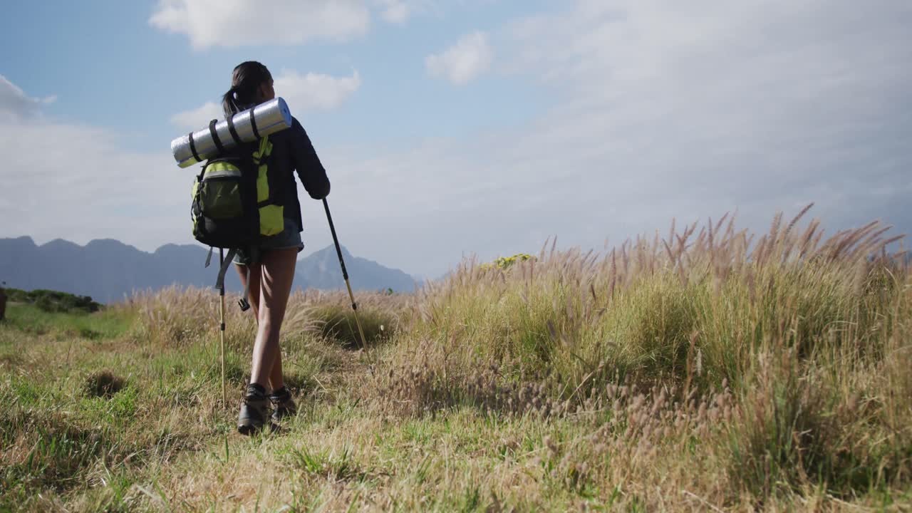 mujer de raza mixta con mochila usando palos nórdicos caminando en el campo