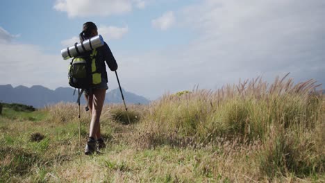 mixed race woman wearing backpack using nordic walking poles hiking in countryside