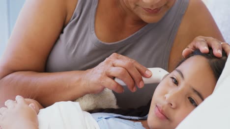 Grandmother-checking-body-temperature-of-sick-granddaughter-in-bed-room-4k