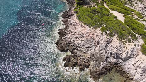 los kayakistas navegan por las aguas cristalinas de cala agulla, mostrando la hermosa costa rocosa y la exuberante vegetación.