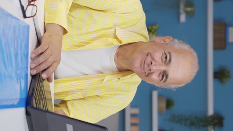 Vertical-video-of-Home-office-worker-old-man-winks-at-camera.