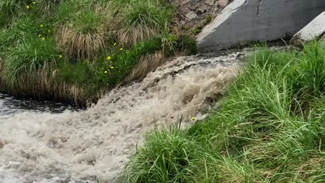 fast-flowing dirty water gushing into the river through a canal