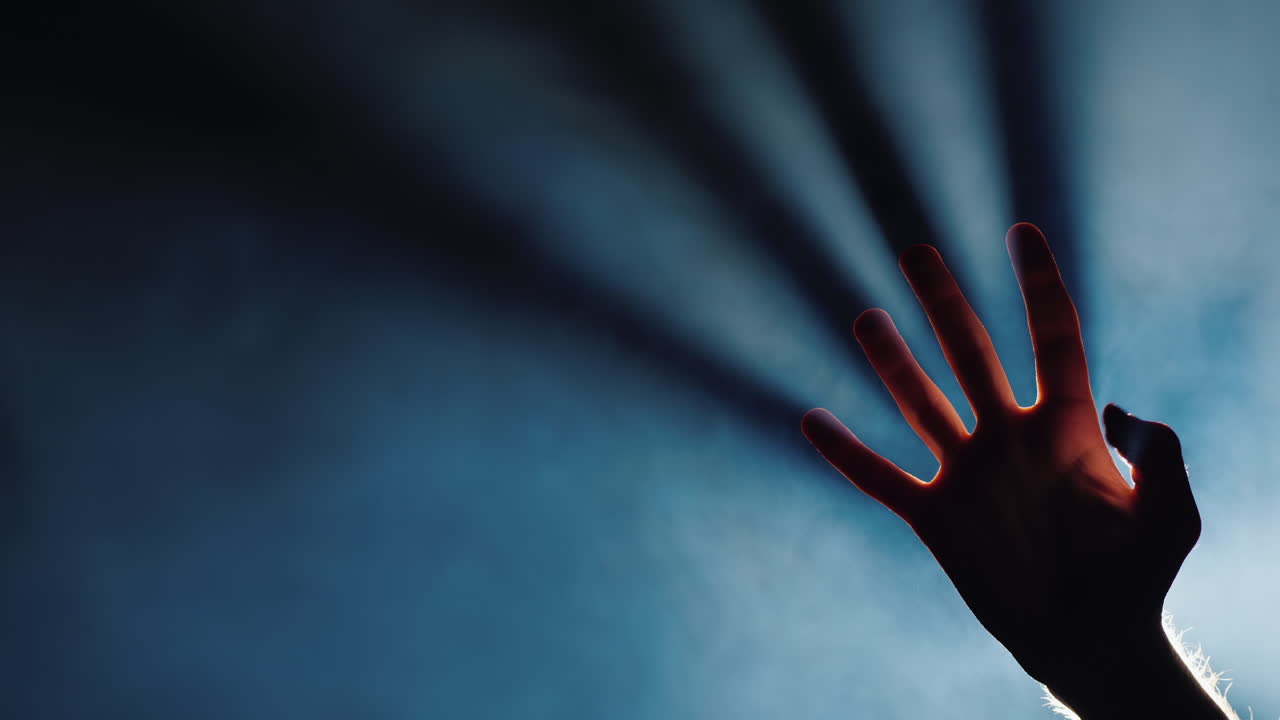 la silueta de la mano de un hombre en la oscuridad de los dedos vienen los rayos de luz