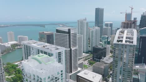 aerial view of downtown skyscrapers on sunny day. slide and pan shot of modern high rise office or apartment buildings and water in background. miami, usa