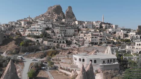 aerial view of road leading into cappadocia, turkey and homes built into the hillside with stone mountain peak in distance and blue sky background