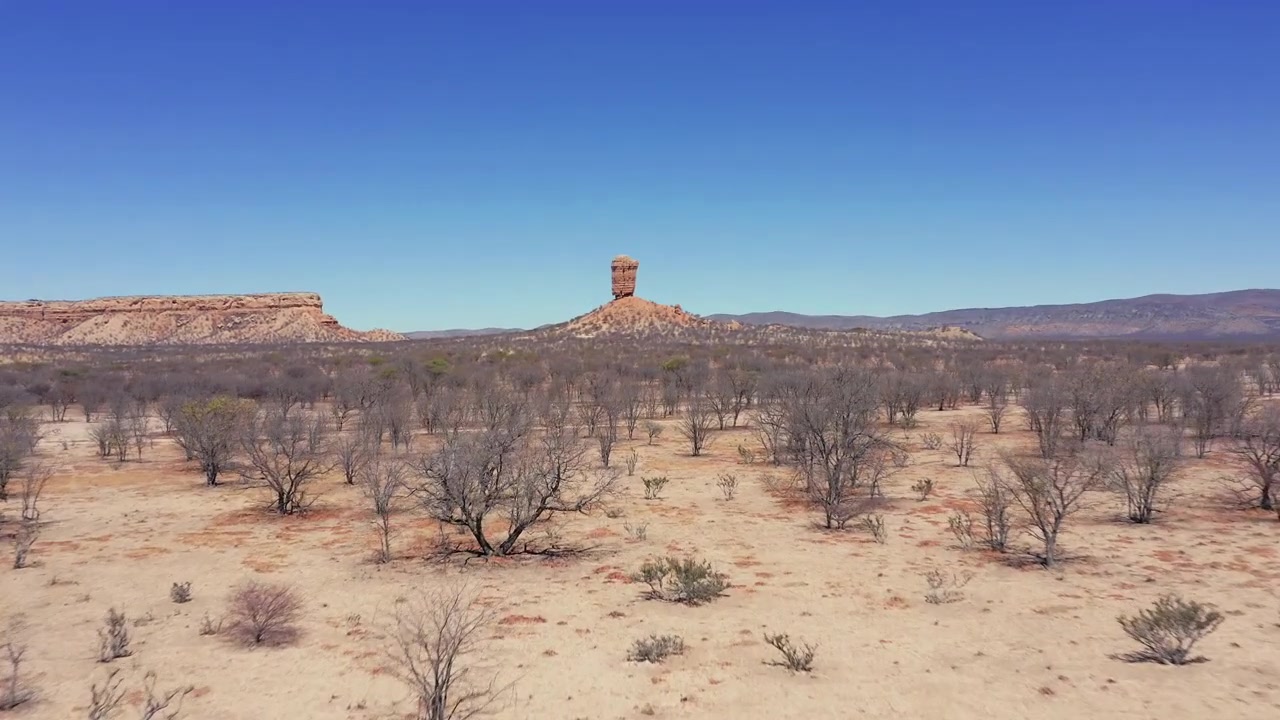 Ripresa panoramica con drone della formazione rocciosa di Fingerklippe in Namibia a mezzogiorno, che mostra l'iconica guglia di roccia circondata da terreno arido e alberi spogli sotto un cielo azzurro e limpido