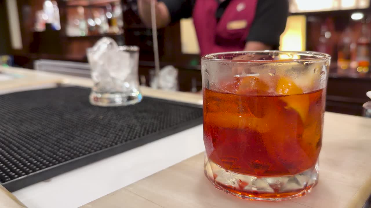 Il barista mescola un cocktail Negroni in un bicchiere con ghiaccio, illuminazione calda, messa a fuoco selettiva, telecamera fissa