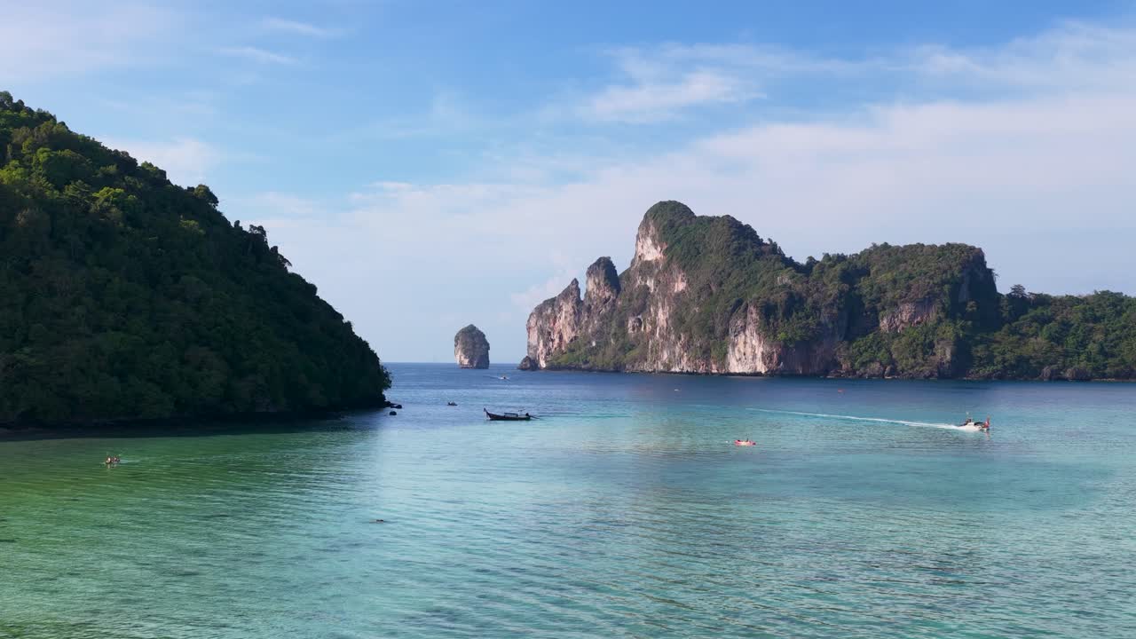 Inquadratura grandangolare statica di scogliere calcaree tropicali e barche longtail su acqua oceanica turchese calma.