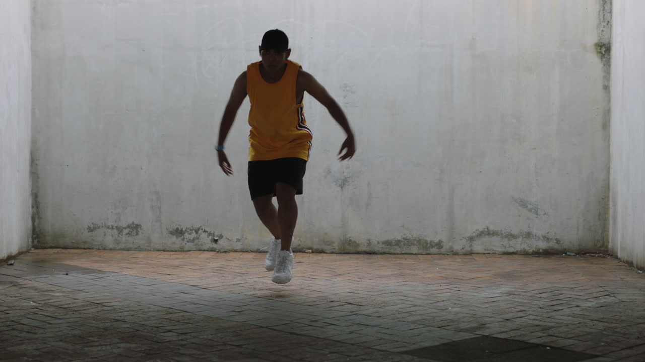 hombre bailarín joven bailarín de calle feliz realizando varios movimientos de baile de estilo libre adecuado hombre de raza mixta practicando en un almacén grungy con chaleco amarillo