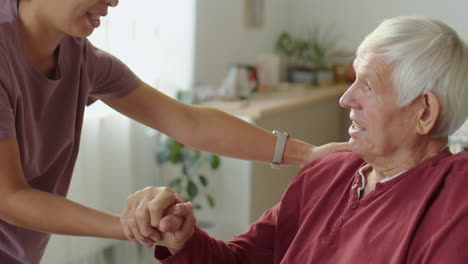 woman holding hands and talking with old man in wheelchair