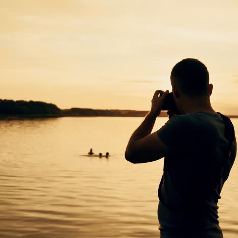man with a camera in his hands makes a photo of the river on the background of sunset