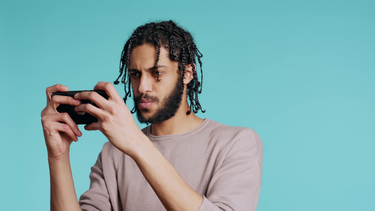 hombre asintiendo con la cabeza, molesto después de perder un videojuego, jugando al teléfono en el estudio