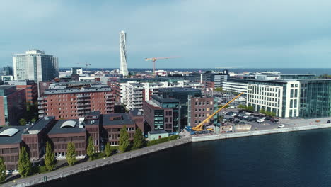 drone aerial shot of cityscape turning torso building skyscraper in malmö sweden harbor at a construction building site near the seaside water with a large crane moving pieces of wood building blocks