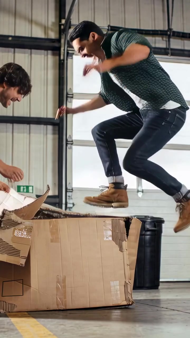 Vertical video: Stepping man in green tee jumping on box in bay breaking box to get packing paper