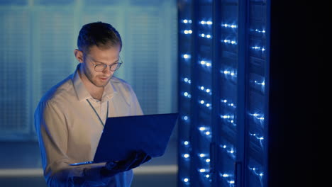 male server engineer in data center. it engineer inspecting a secure server cabinet using modern technology laptop coworking in data center.