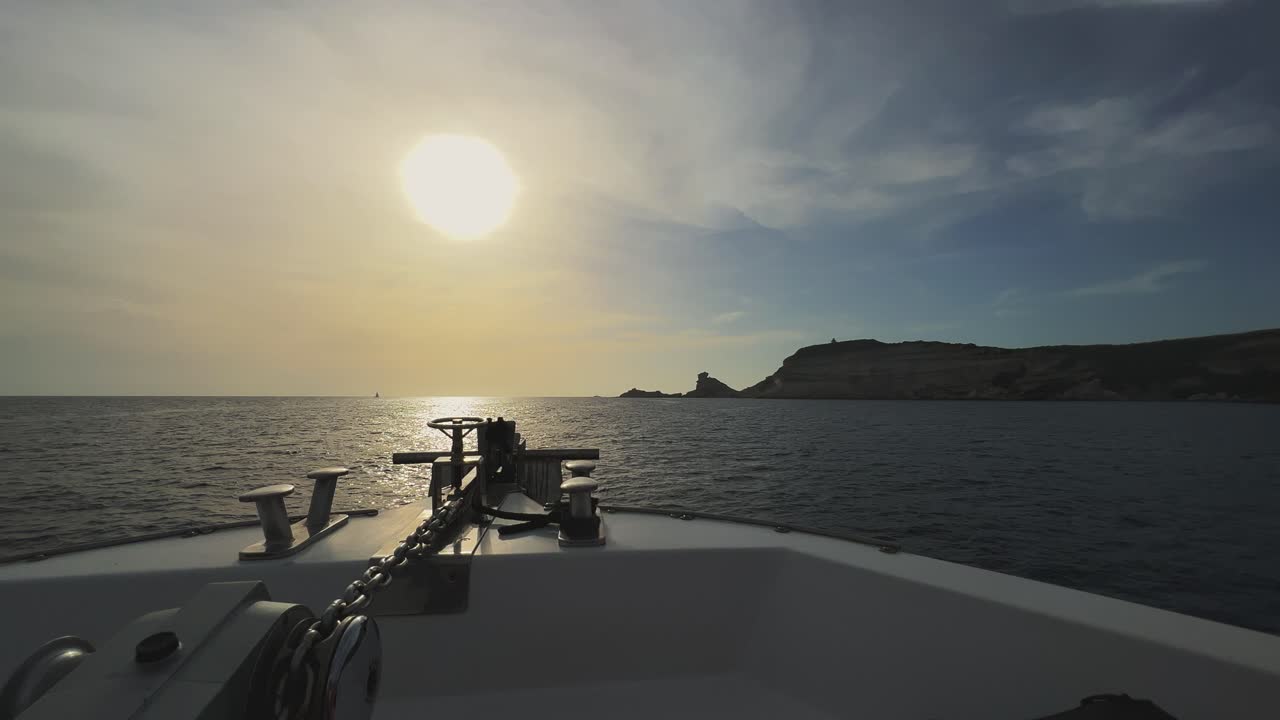 punto de vista de la proa del velero navegando hacia los acantilados de la isla de córcega y el faro de capo pertusato en francia con el sol de fondo al atardecer, imágenes horizontales de 50 fps