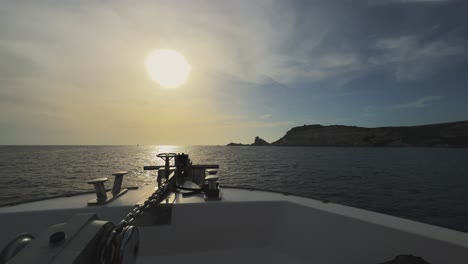 point of view of sailboat bow navigating toward corsica island cliffs and capo pertusato lighthouse in france with sun in background at sunset, 50fps horizontal footage