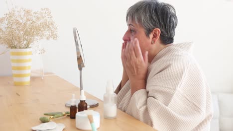 Elderly-woman-in-bathrobe-applying-facial-cream