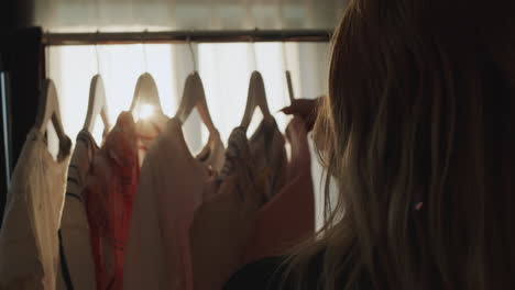 woman chooses a dress in the dressing room, back view in the rays of the sun