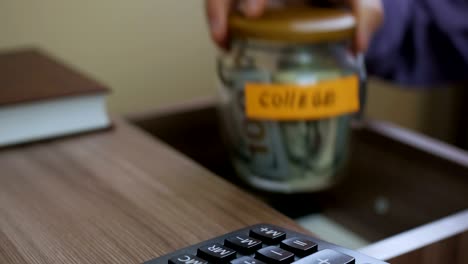 caucasian male putting a glass jar put in a drawer  table with his savings for future college