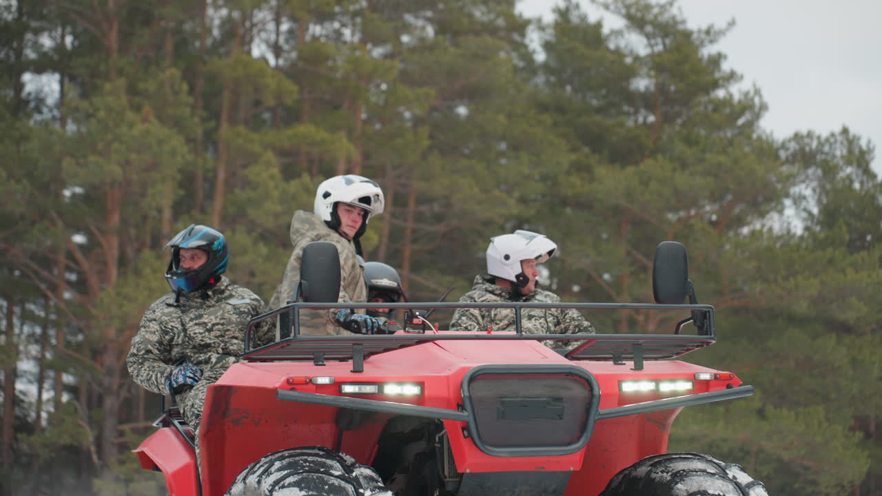 Tre piloti guidano un ATV rosso sulla neve con uno sfondo di pineta, pneumatici ad alta trazione che scolpiscono la neve, un'inquadratura frontale in movimento cattura velocità, slancio e coordinazione di squadra, paesaggio invernale e veicolo.