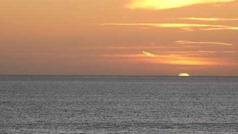 puesta de sol en el mar, gran disco rojo del sol se mueve detrás del océano con algunas nubes