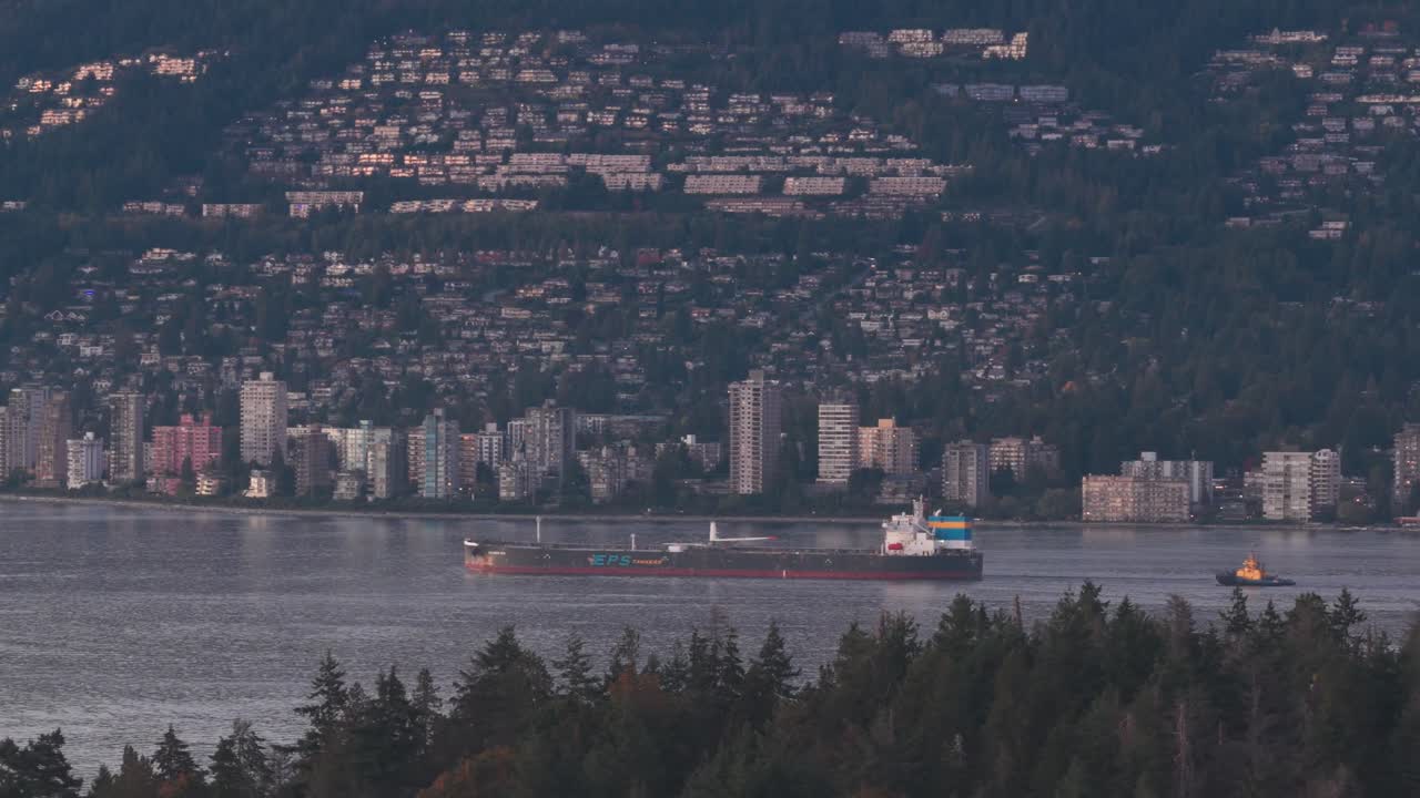 Aerial telephoto dolly shot of a barge sailing past West Vancouver on a clear evening in British Columbia, Canada. 4K