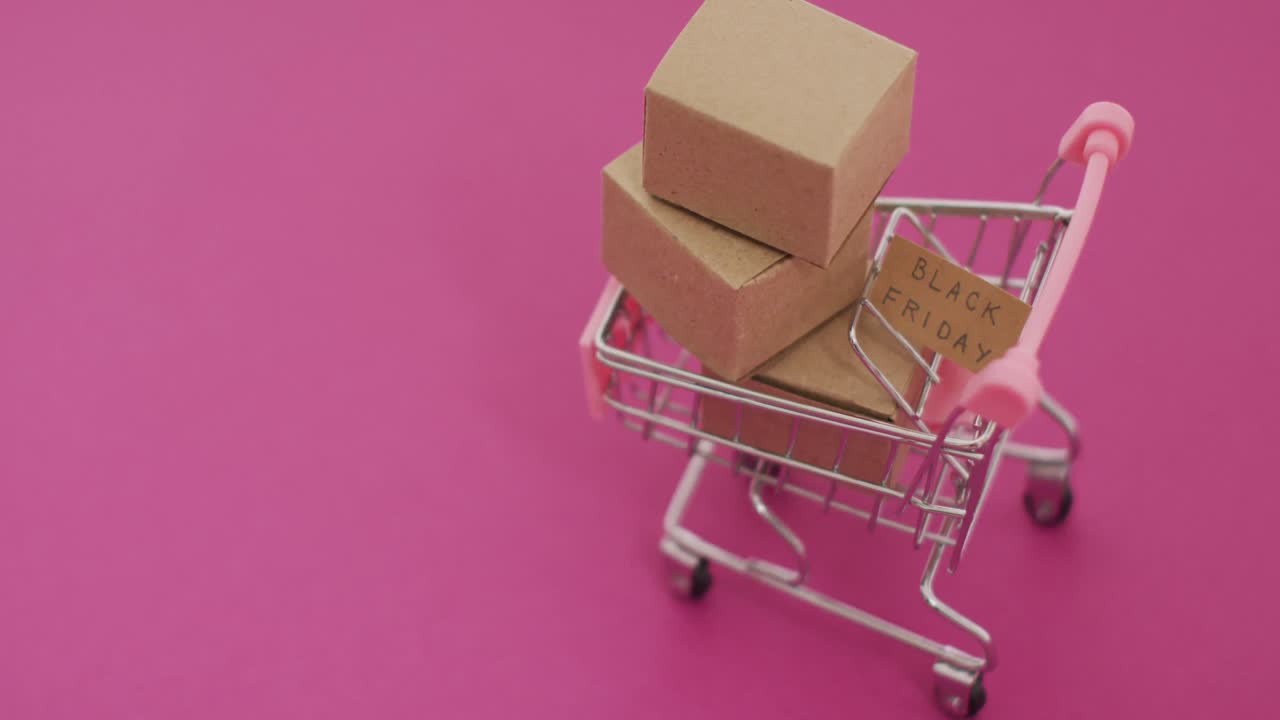 video del texto del viernes negro en cartón y cajas en el carrito de compras sobre fondo rosa