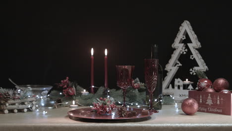 un hombre toma un vaso rojo de una mesa de navidad decorada en una habitación oscura