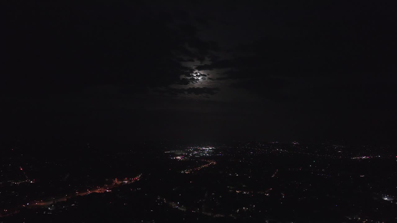 Video di un drone che riprende un paesaggio urbano illuminato da una super luna e dalle luci della città di notte. La visuale aerea offre una prospettiva mozzafiato, mettendo in risalto la serena atmosfera notturna.
