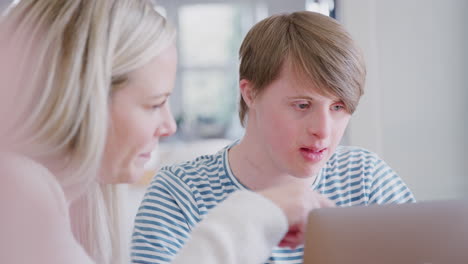 Mann-Mit-Down-Syndrom-Sitzt-Mit-Einer-Nachhilfelehrerin-Zusammen-Und-Nutzt-Laptop-Für-Den-Unterricht-Zu-Hause