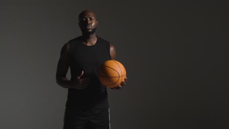 studio portrait shot of male basketball player throwing ball from hand to hand against dark background 1