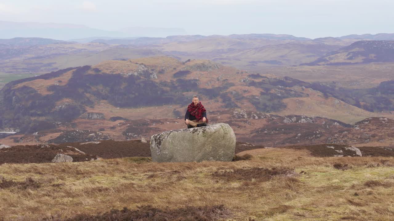 hombre meditando en la naturaleza salvaje en una gran roca en posición de loto en el paisaje rural de escocia, tierras altas del oeste