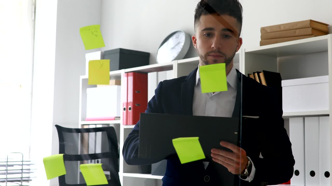 businessman making notes in documents standing near glass wall